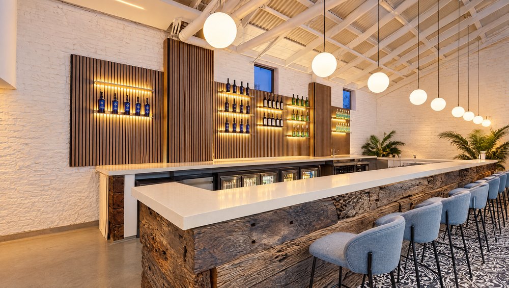 The bar in the evening, running the length of the room, stools along it and the lit shelves behind