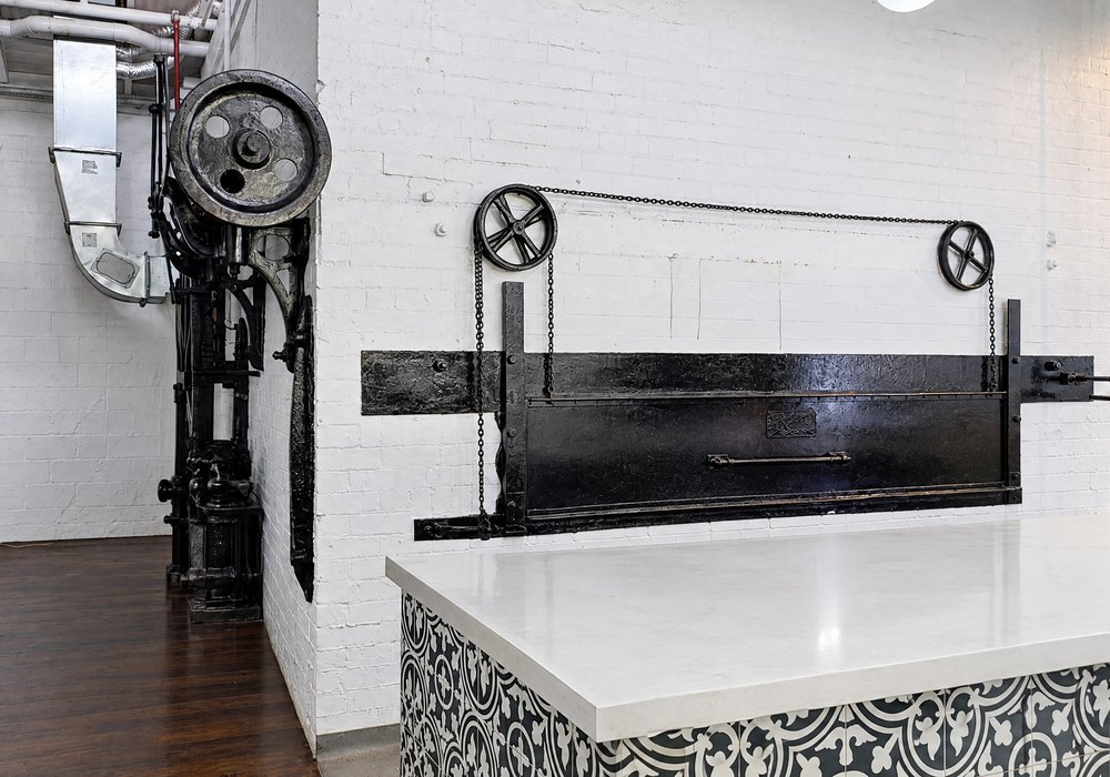 The steak oven: a long black cast iron door set low in a white brick wall, with two iron wheels and a chain above it